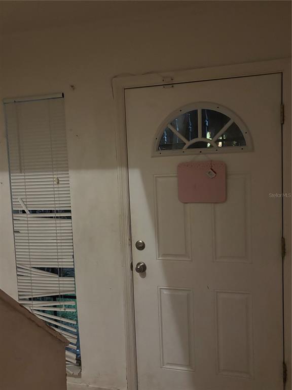 A white front door with a semi-circular window sits next to a damaged vertical window blind — 3401 SUNRISE VILLAS COURT S, TAMPA, FL