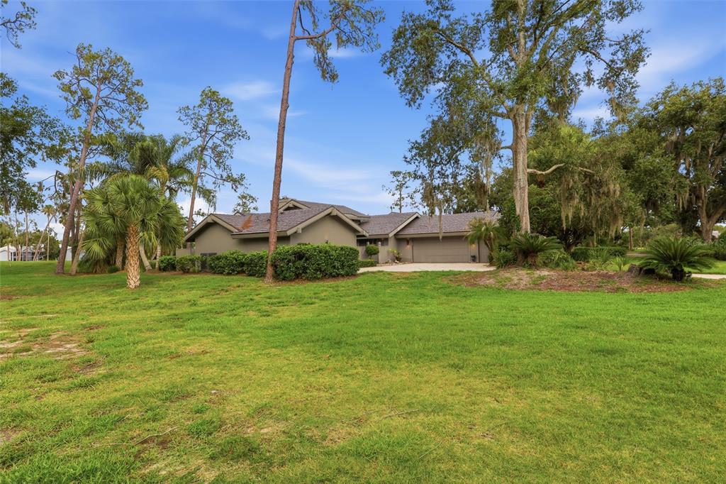 A single-story house with a gray roof and garage sits on a large grassy lawn — 5434 KEMKERRY ROAD, WESLEY CHAPEL, FL