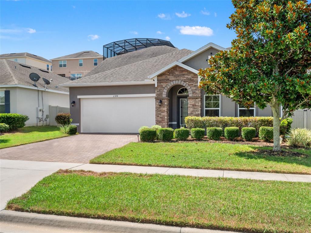 A single-story house with a stone-accented entryway, a two-car garage, and a screened pool enclosure — 2394 HASTINGS BOULEVARD, CLERMONT, FL