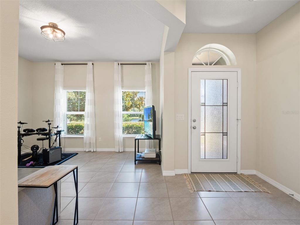 A bright entryway with tile flooring, a front door with glass panels, and a drum set — 2394 HASTINGS BOULEVARD, CLERMONT, FL