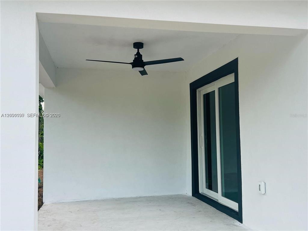 A covered patio features a black ceiling fan, white walls, and a sliding glass door — 1125 MILWAUKEE BOULEVARD, LEHIGH ACRES, FL