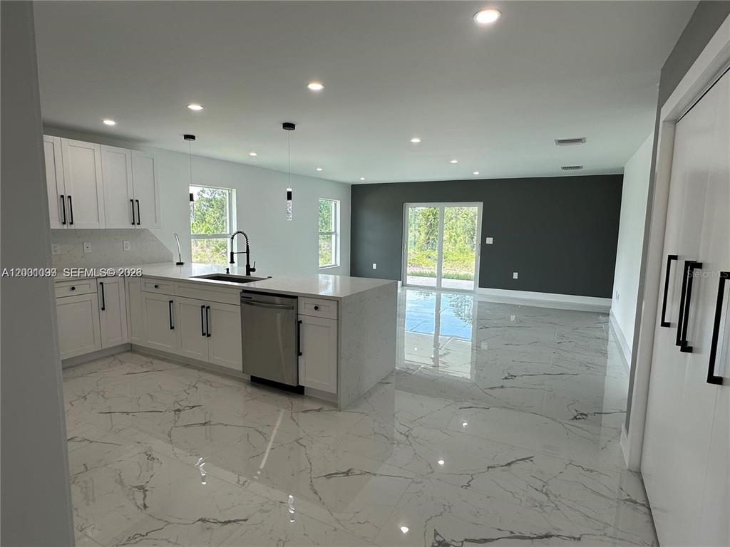 A modern kitchen with white cabinets and a marble-patterned floor opens to a living area — 1125 MILWAUKEE BOULEVARD, LEHIGH ACRES, FL