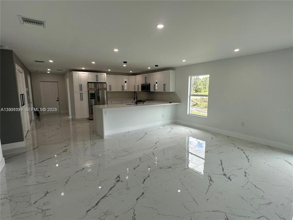 A modern kitchen features white cabinetry, stainless steel appliances, and polished marble-look tile flooring — 1125 MILWAUKEE BOULEVARD, LEHIGH ACRES, FL