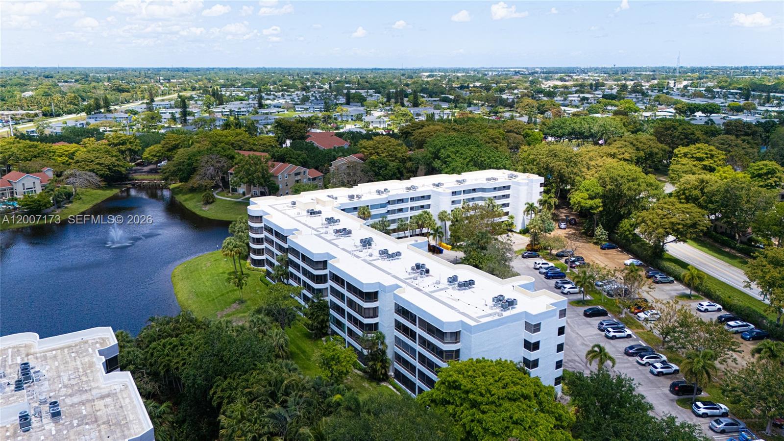 An aerial view shows a multi-story white apartment building situated next to a lake — 1850 Homewood Blvd # 5010, Delray Beach FL 33445, DELRAY BEACH, FL