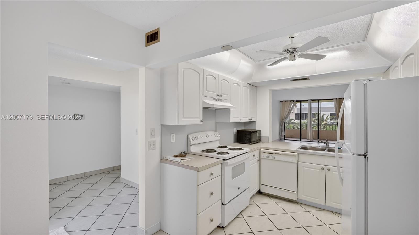A white kitchen features tile flooring, white cabinetry, and a view of a balcony — 1850 Homewood Blvd # 5010, Delray Beach FL 33445, DELRAY BEACH, FL