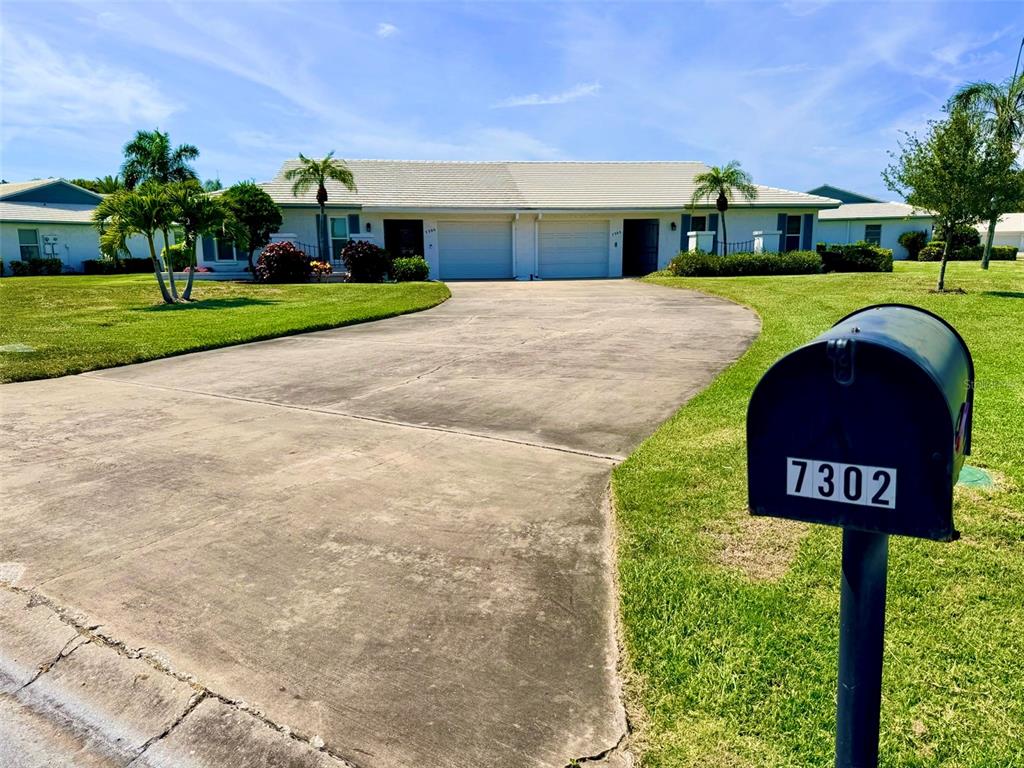 A single-story duplex with a concrete driveway and a mailbox in the foreground — 7302 9TH AVENUE W UNIT 7302, BRADENTON, FL