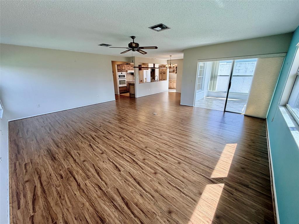 A spacious living room features wood-look tile flooring, a ceiling fan, and sliding glass doors — 7302 9TH AVENUE W UNIT 7302, BRADENTON, FL