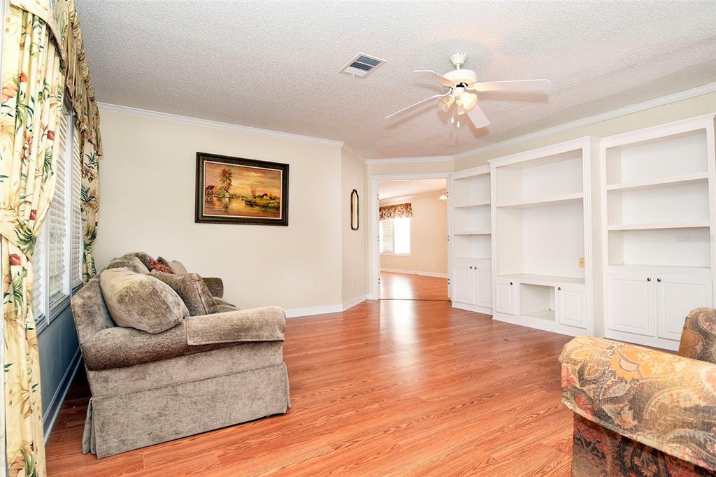 A living room with wood-look flooring, a ceiling fan, built-in shelving, and a sofa — 11642 MARTELL COURT, LEESBURG, FL