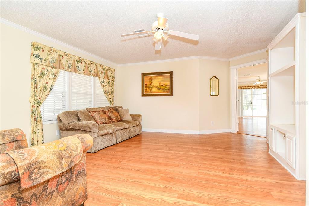 A living room with wood-look flooring, a beige sofa, a ceiling fan, and built-in shelving — 11642 MARTELL COURT, LEESBURG, FL