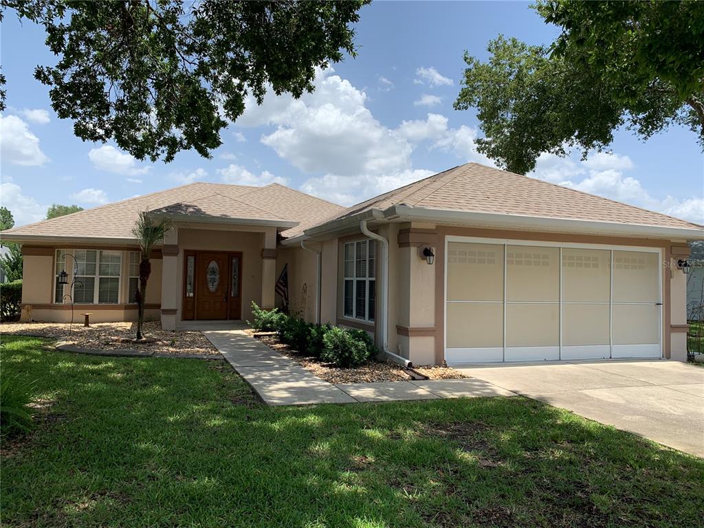 A single-story house with a beige stucco exterior, a brown shingled roof, and a garage — 6369 SW 117TH LOOP, OCALA, FL