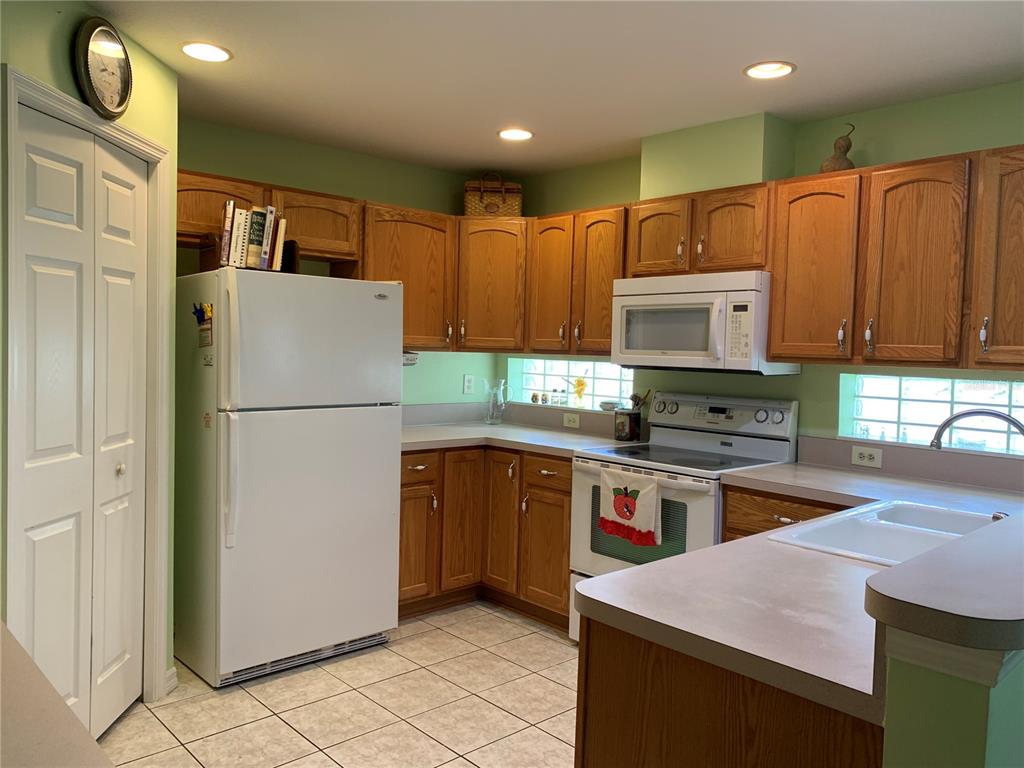 A kitchen with light green walls, oak cabinets, white appliances, and a tiled floor — 6369 SW 117TH LOOP, OCALA, FL