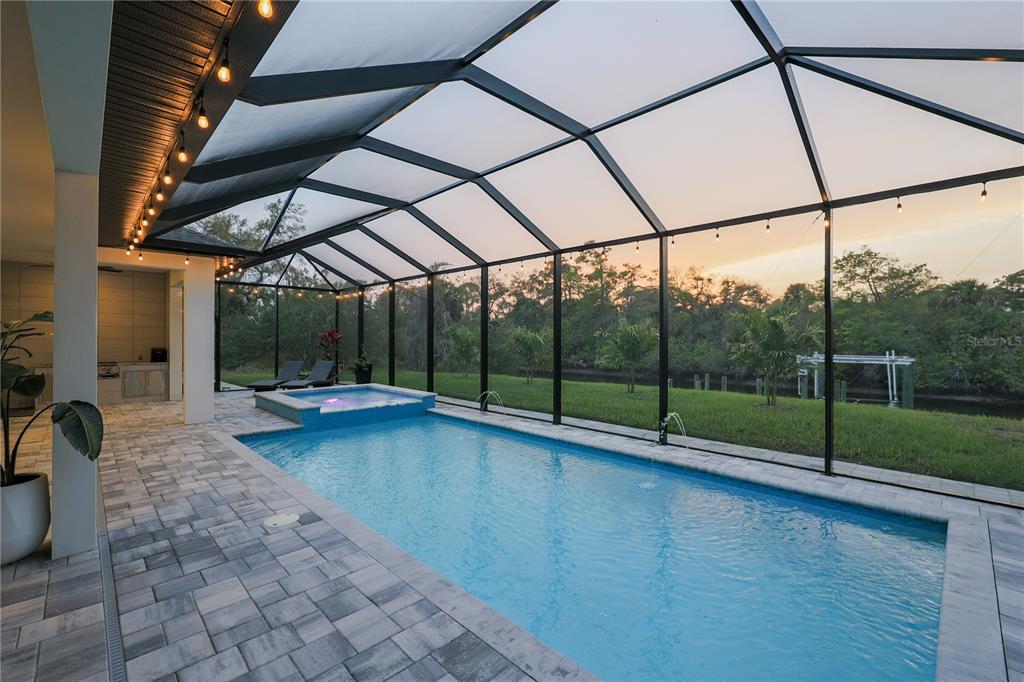A screened-in pool and spa area with a paved deck overlooking a grassy backyard — 1015 HOFFER STREET, PORT CHARLOTTE, FL