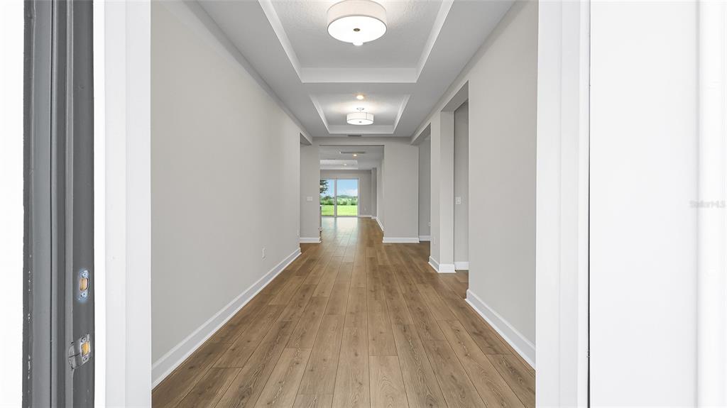 A long hallway with light wood flooring leads toward a glass door with outdoor views — 1613 BELLAGIO LOOP, TAVARES, FL