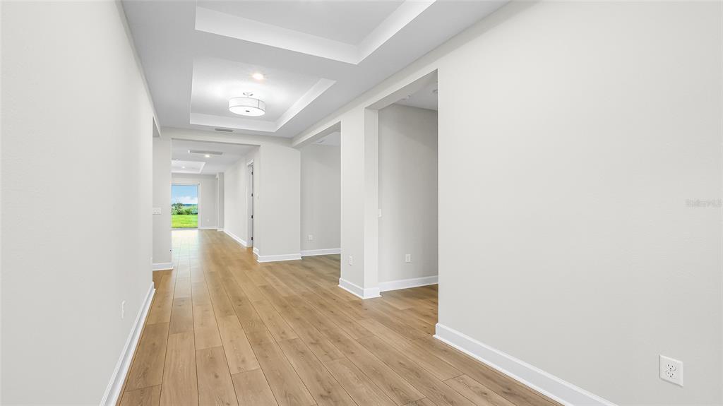 A long hallway with light wood flooring leads toward a bright room with a view — 1613 BELLAGIO LOOP, TAVARES, FL