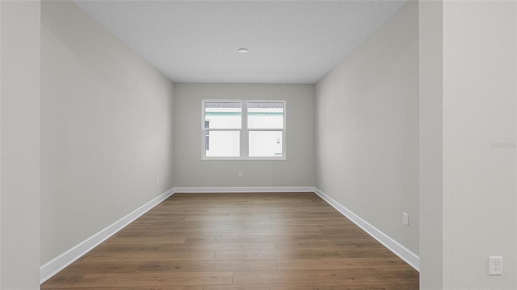 An empty room with light gray walls, wood-look flooring, and a window — 1613 BELLAGIO LOOP, TAVARES, FL