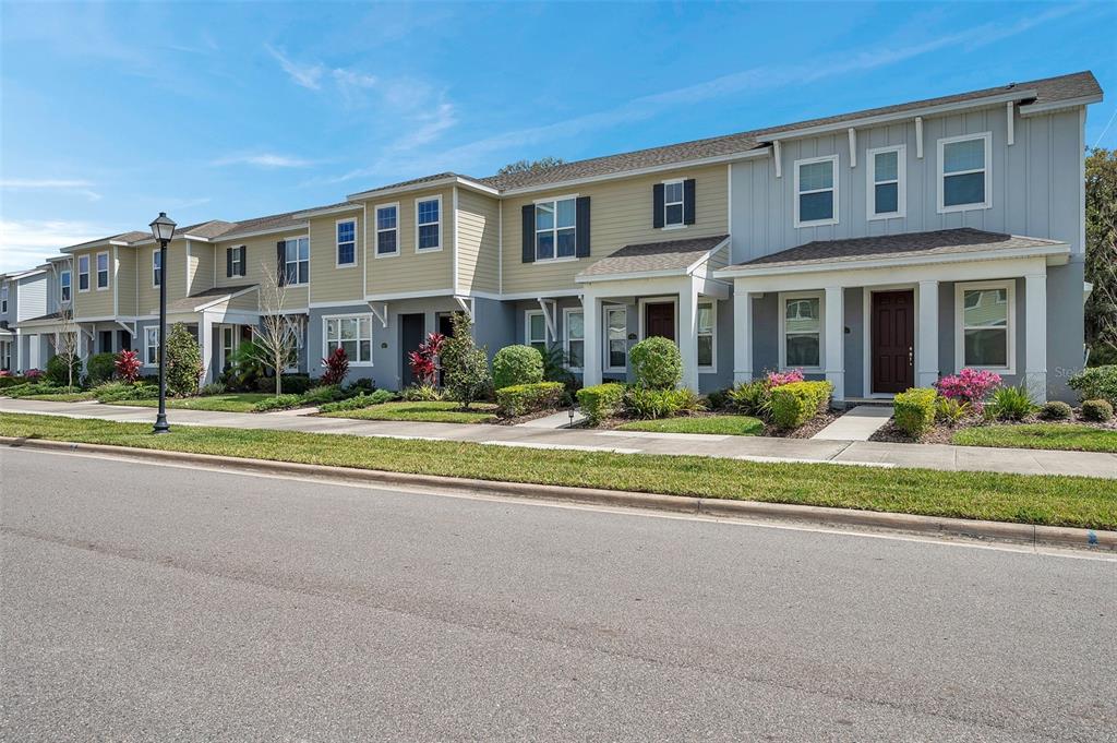 A row of two-story townhomes with light-colored siding and gray lower levels under a blue sky — 4966 AVALON PARK BOULEVARD, WESLEY CHAPEL, FL