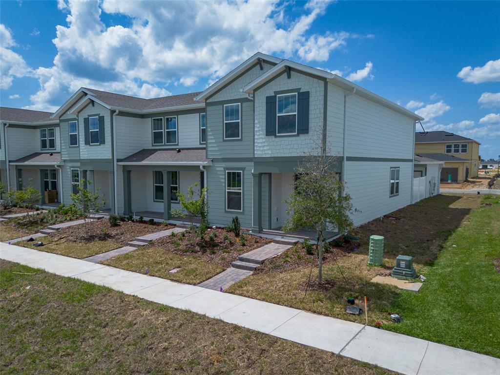 An exterior view of a two-story townhouse with light green siding and a paved walkway — 4565 ORCHARD VIEW ALLEY, CLERMONT, FL
