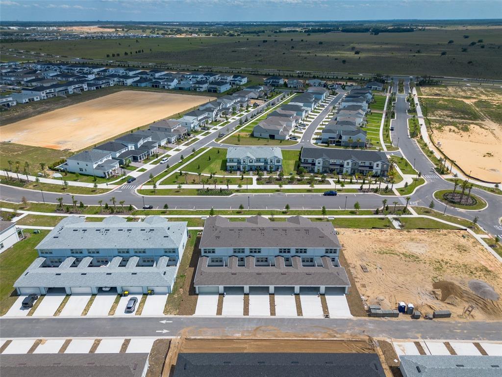 An aerial view shows multiple rows of townhomes and suburban streets under construction — 4565 ORCHARD VIEW ALLEY, CLERMONT, FL