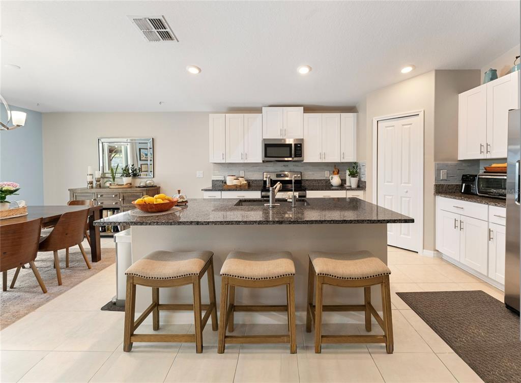 A kitchen features white cabinets, granite countertops, a central island with bar stools, and tile flooring — 36548 GARDEN WALL WAY, ZEPHYRHILLS, FL