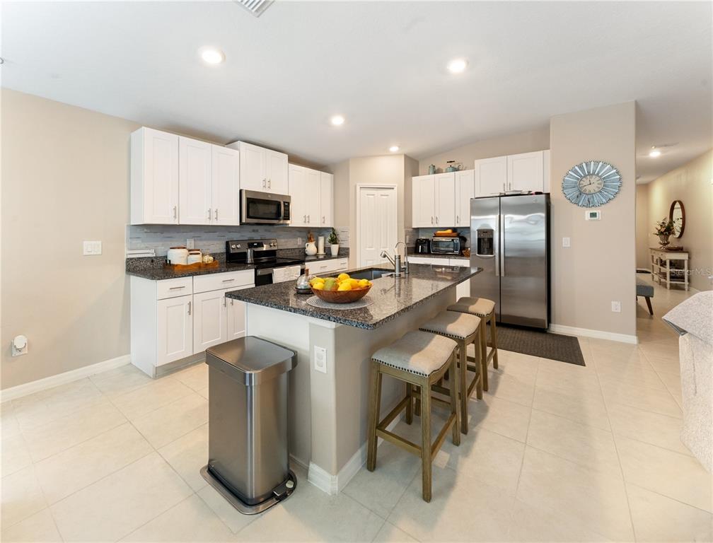 A kitchen features white cabinets, granite countertops, a center island with seating, and stainless appliances — 36548 GARDEN WALL WAY, ZEPHYRHILLS, FL