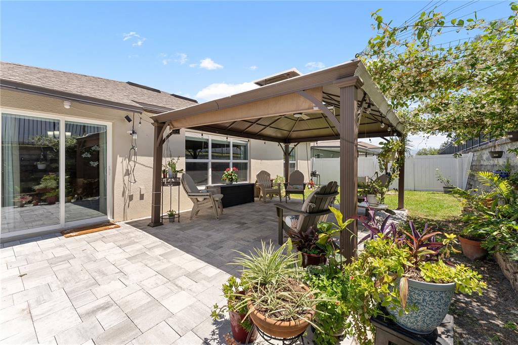 A backyard patio features a metal gazebo, stone pavers, and several potted plants — 36548 GARDEN WALL WAY, ZEPHYRHILLS, FL