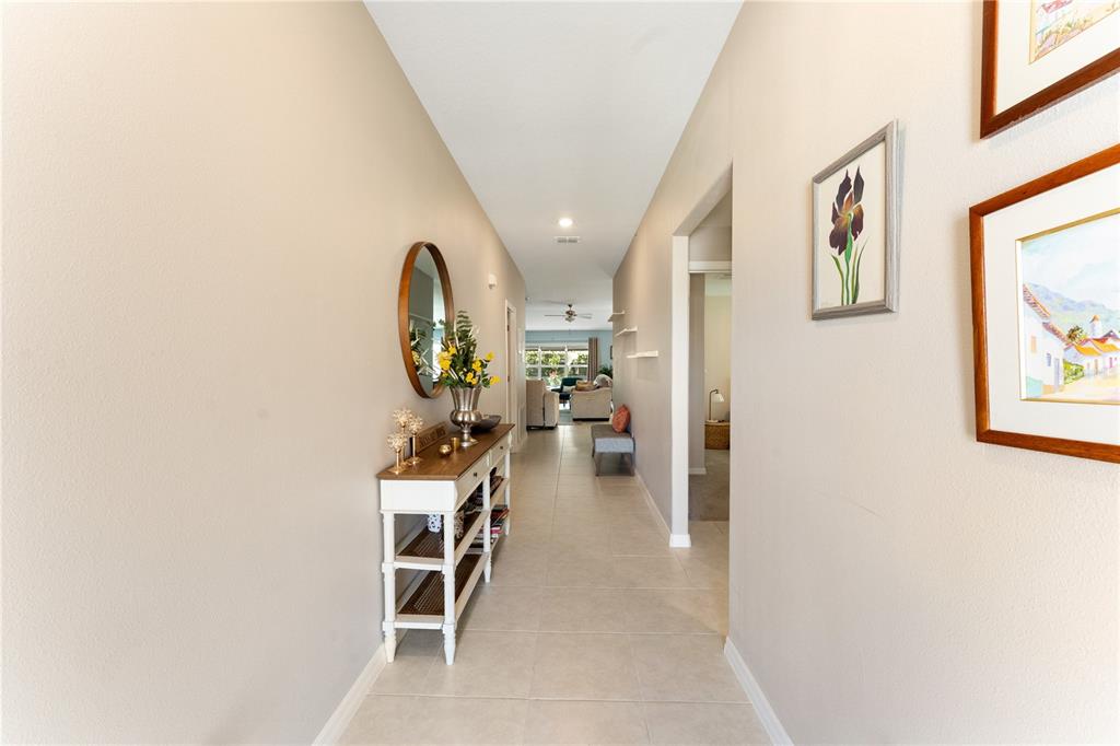 A hallway with tile flooring leads to a living area featuring a console table — 36548 GARDEN WALL WAY, ZEPHYRHILLS, FL