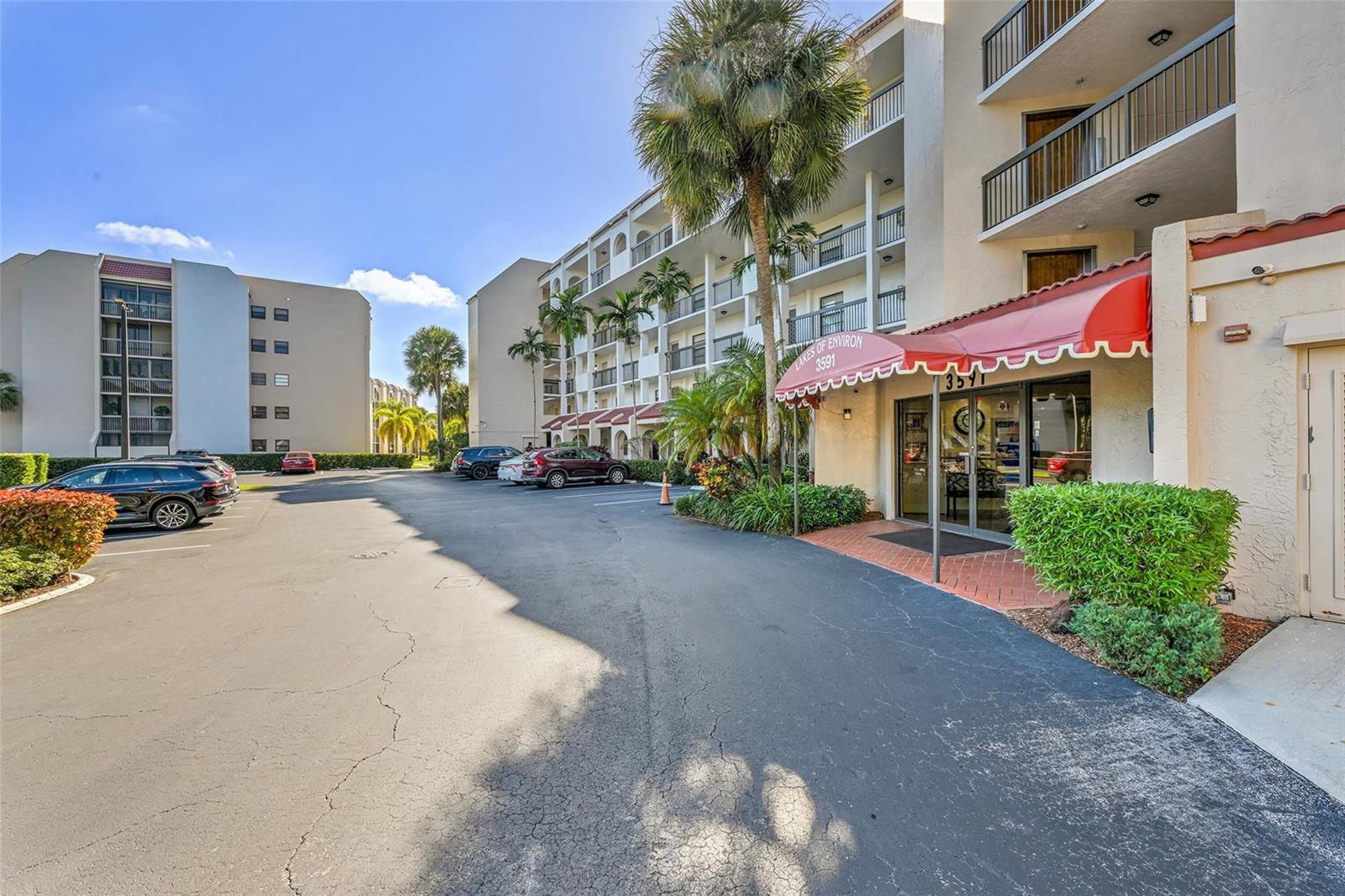 The exterior of a multi-story apartment building features a red awning over the main entrance — 3591 Environ Boulevard # A305, Lauderhill FL 33319, LAUDERHILL, FL