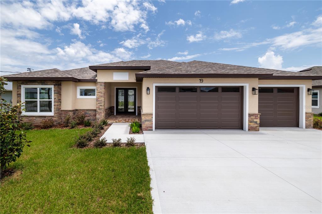 A single-story house with a tan stucco exterior, stone accents, and a three-car garage — 19 FRANCIS LANE, PALM COAST, FL
