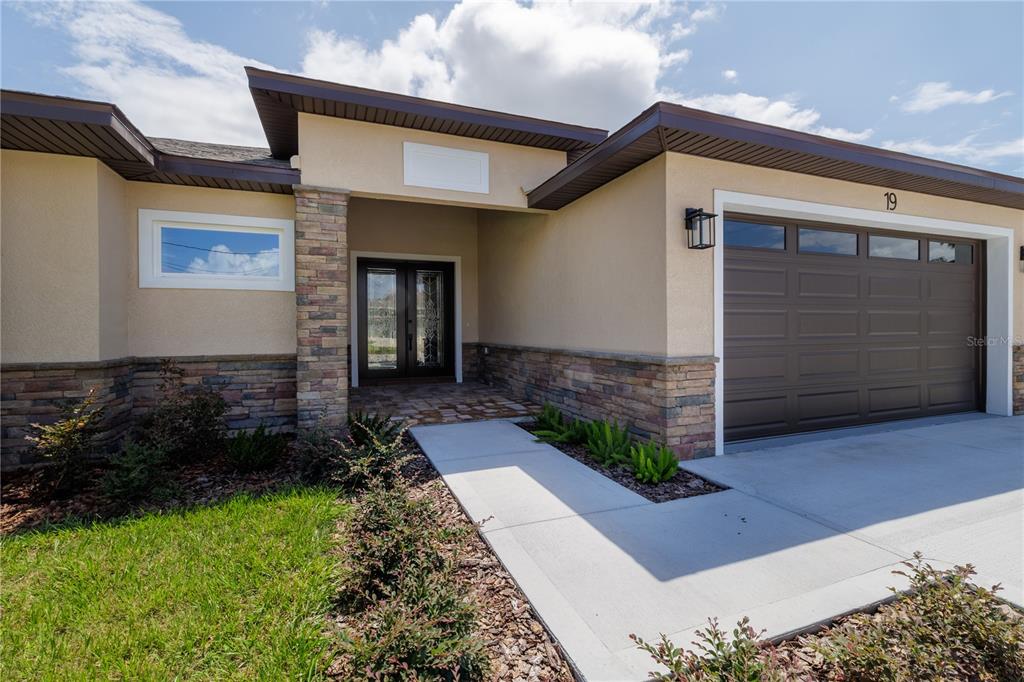 The exterior of a house features a stone facade, a brown garage door, and a walkway — 19 FRANCIS LANE, PALM COAST, FL