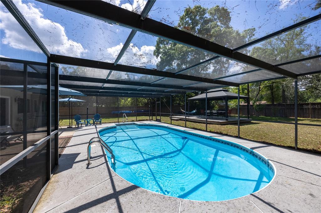 An oval swimming pool is enclosed by a screened lanai in a backyard setting — 5016 NW 36TH STREET, GAINESVILLE, FL