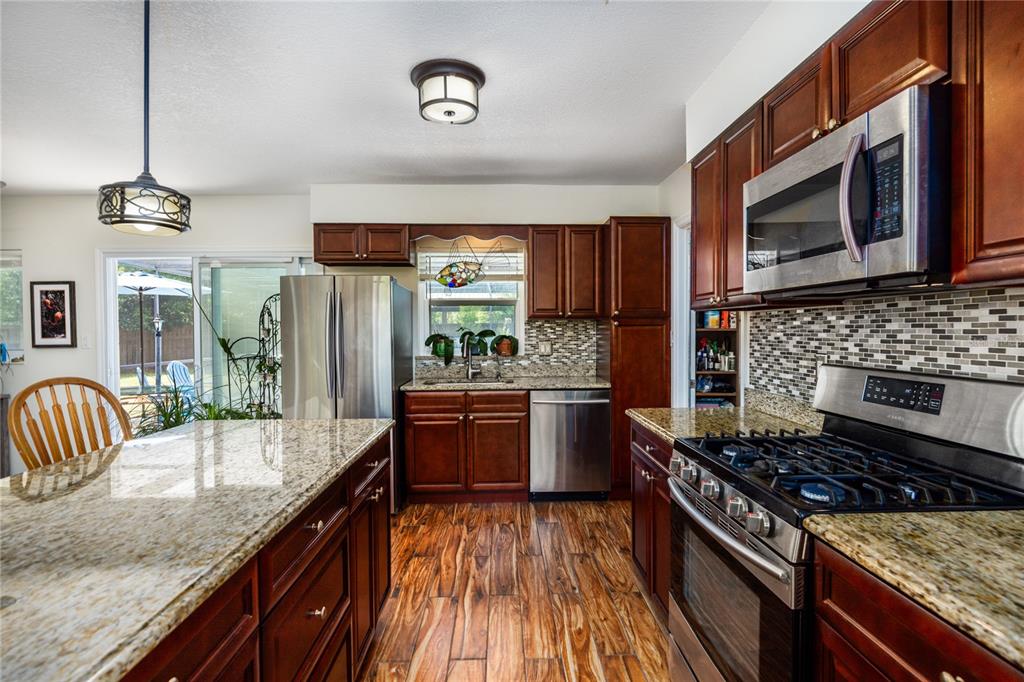 A kitchen features dark wood cabinets, granite countertops, stainless steel appliances, and wood-look flooring — 5016 NW 36TH STREET, GAINESVILLE, FL