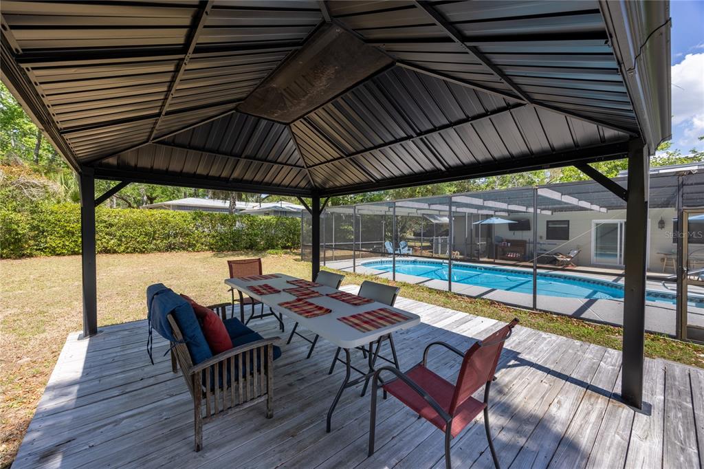 A covered wooden deck features a dining table and chairs overlooking a screened-in swimming pool — 5016 NW 36TH STREET, GAINESVILLE, FL