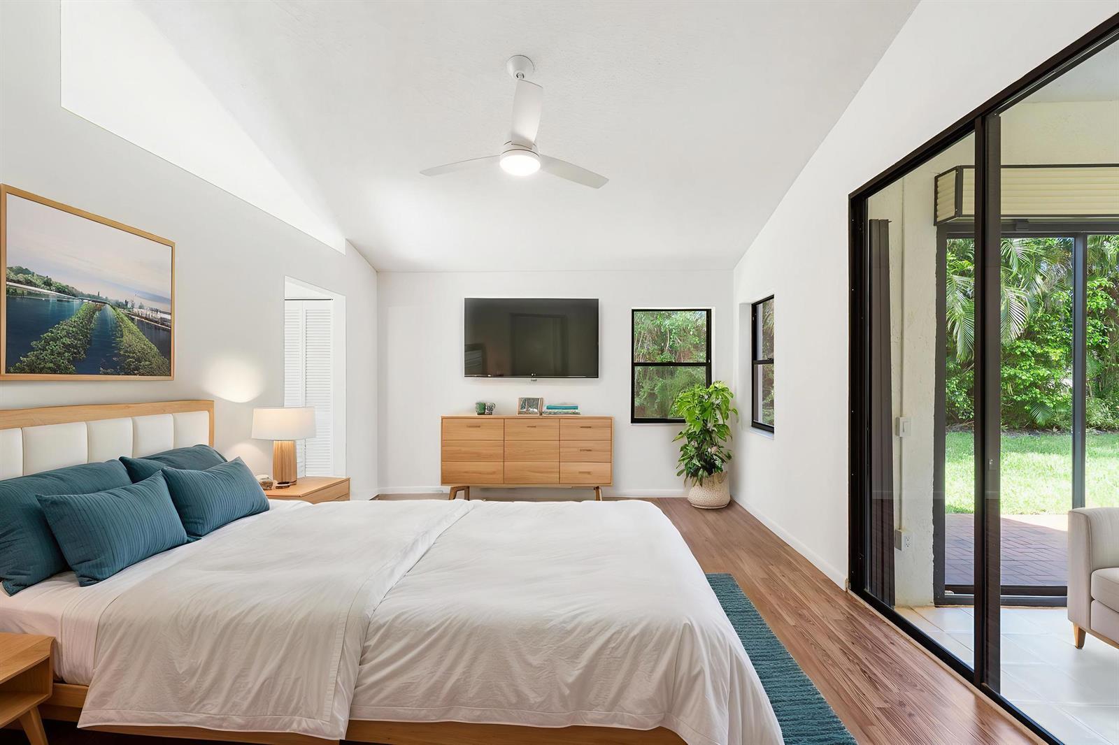 A bedroom with a white bed, wood dresser, ceiling fan, and sliding glass doors outside — 7219 Le Chalet Boulevard, Boynton Beach FL 33472, BOYNTON BEACH, FL