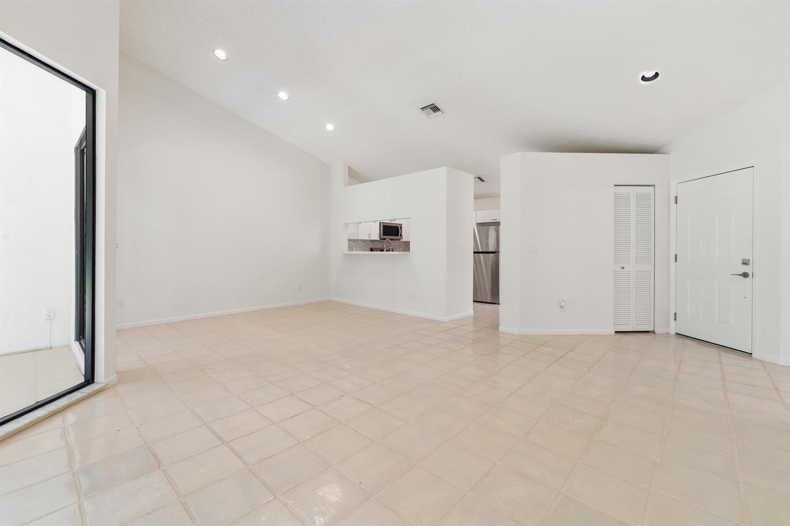 An open-concept living area features vaulted ceilings, beige tile flooring, and a view into the kitchen — 7219 Le Chalet Boulevard, Boynton Beach FL 33472, BOYNTON BEACH, FL