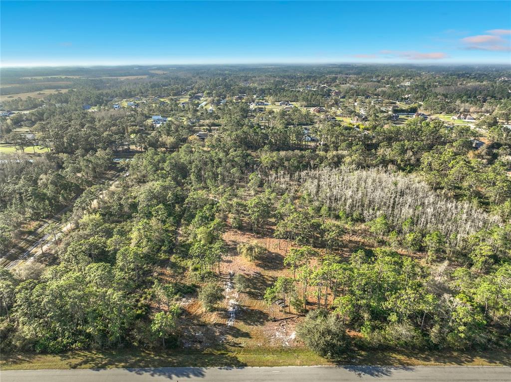 An aerial view shows a wooded lot bordering a paved road under a blue sky — QUARTERLY PARKWAY, ORLANDO, FL
