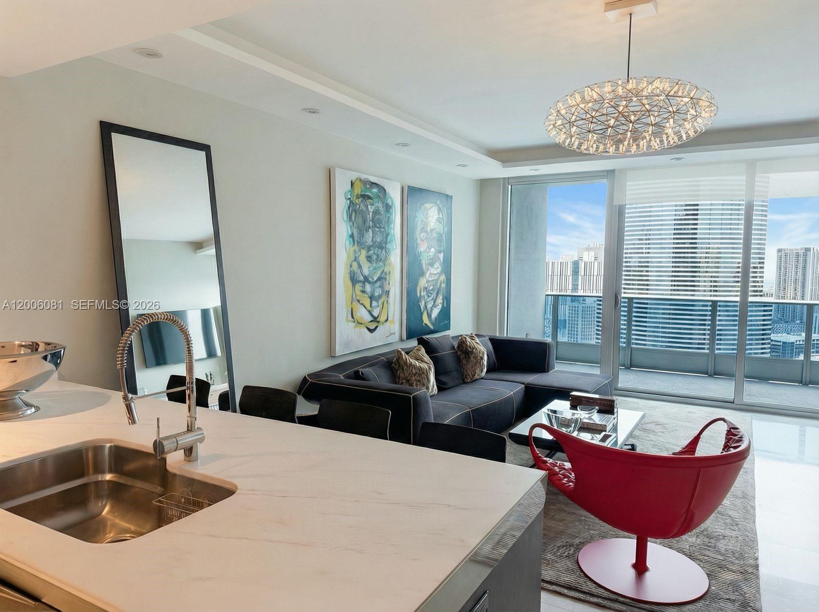 A modern living room and kitchen area features a red chair and city balcony views — 200 BISCAYNE BLVD WAY # 4310, Miami FL 33131, MIAMI, FL