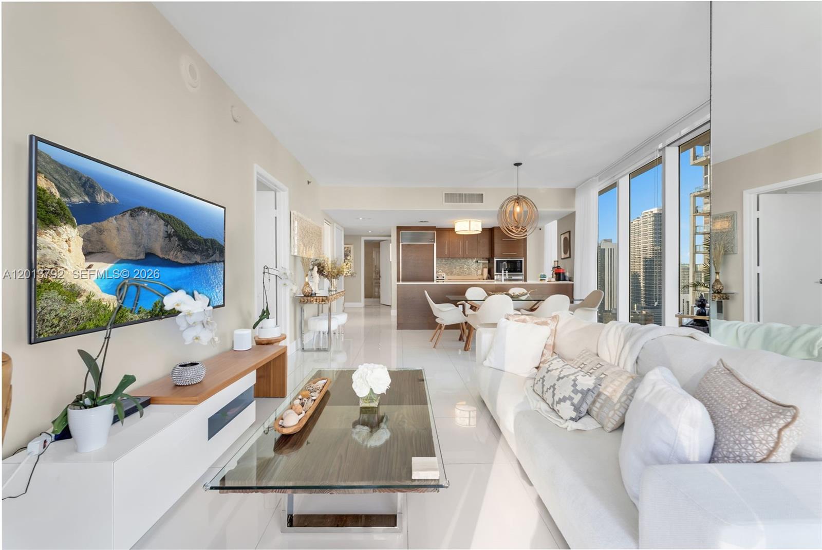 A modern living room and kitchen area features white tile floors, a sofa, and city views — 475 Brickell Ave # 3515, Miami FL 33131, MIAMI, FL