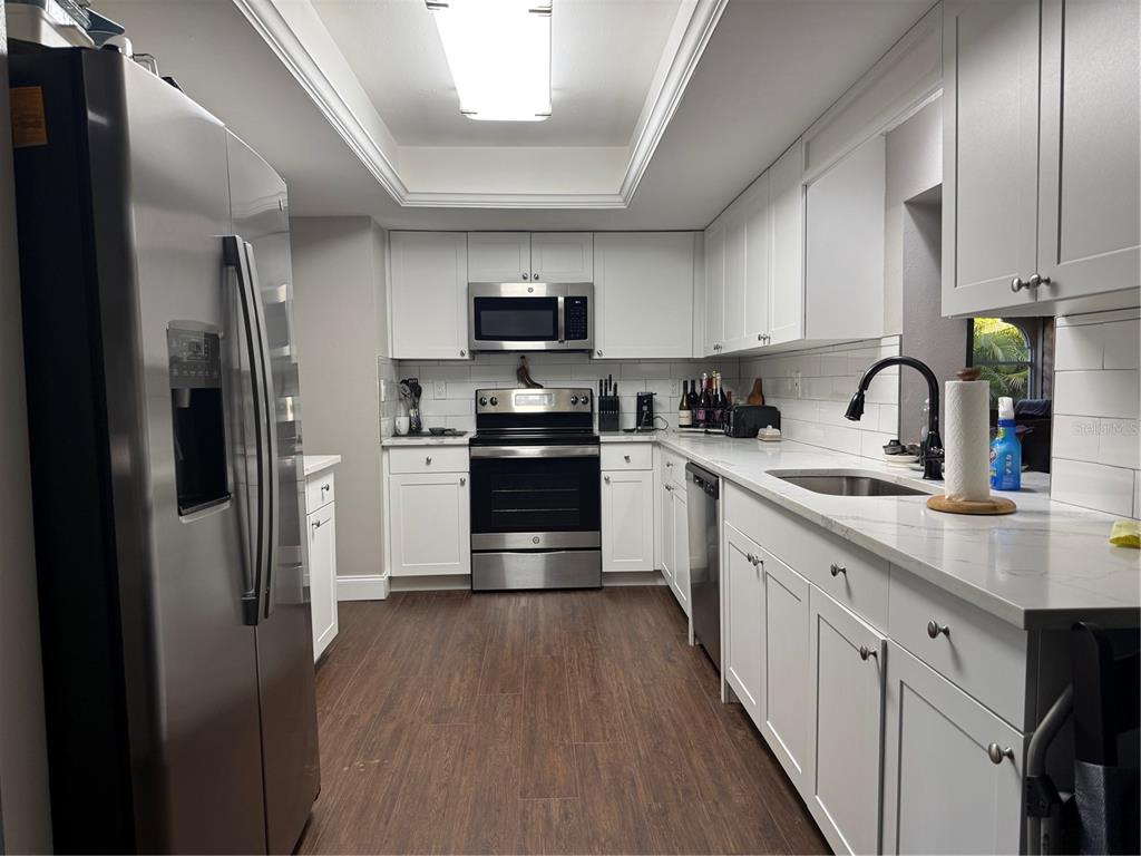A galley kitchen features white cabinets, stainless steel appliances, quartz countertops, and wood-look flooring — 945 CHEVY CHASE STREET, PORT CHARLOTTE, FL