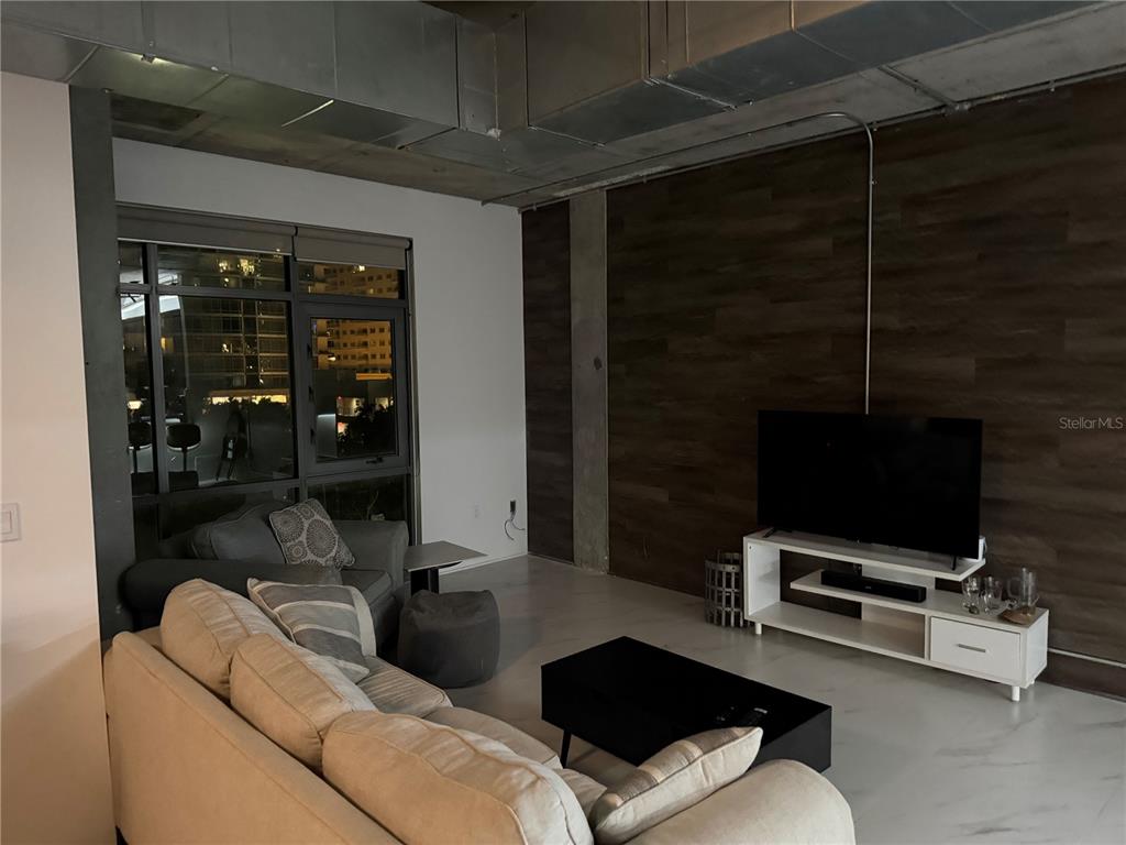 A living room features a wood-paneled accent wall, exposed ductwork, and a large window — 10 N SUMMERLIN AVENUE UNIT 34, ORLANDO, FL