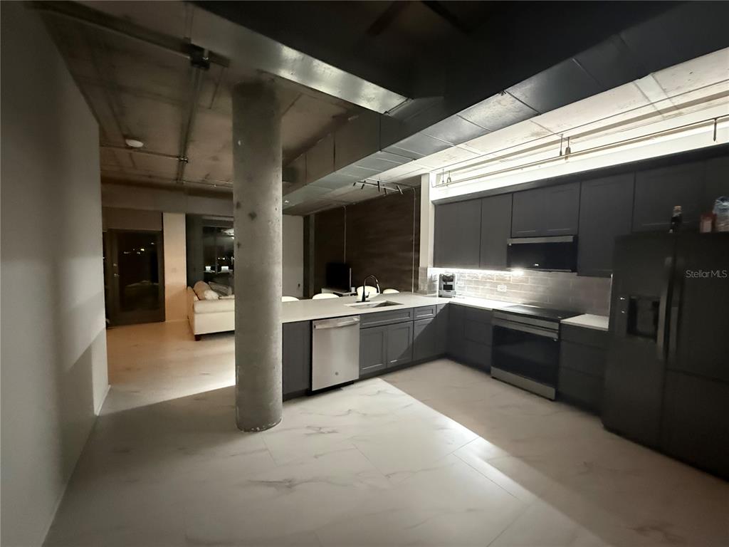 A modern kitchen features dark gray cabinetry, stainless steel appliances, and an exposed concrete ceiling — 10 N SUMMERLIN AVENUE UNIT 34, ORLANDO, FL