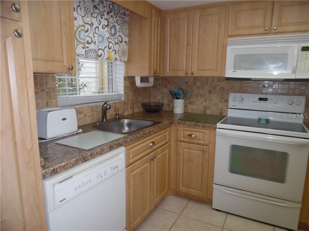 A kitchen features light wood cabinets, granite countertops, a white dishwasher, and a white stove — 1656 S LAKE AVENUE UNIT 3, CLEARWATER, FL