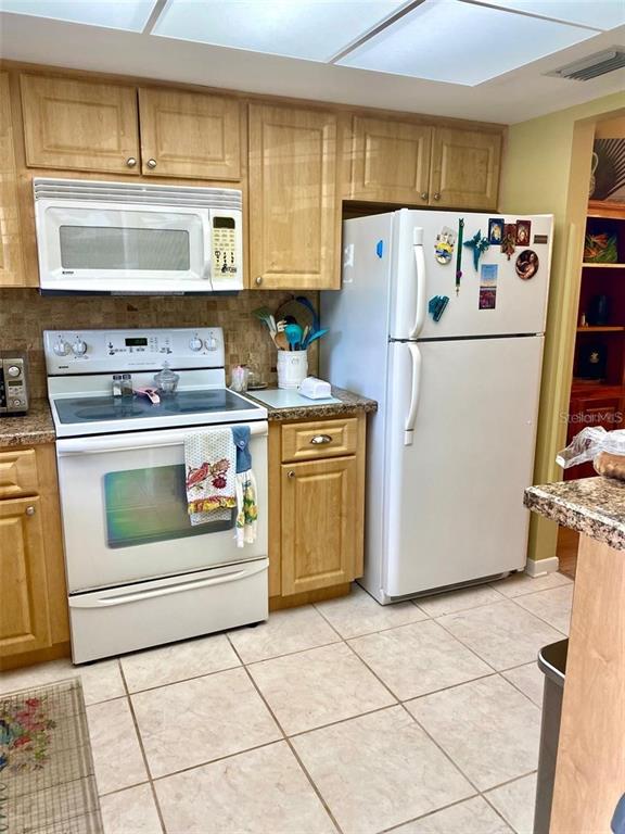 A kitchen features light wood cabinets, white appliances, and beige tile flooring — 1656 S LAKE AVENUE UNIT 3, CLEARWATER, FL