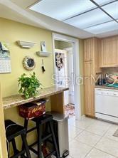 A kitchen features a breakfast bar with two stools, light wood cabinets, and tile flooring — 1656 S LAKE AVENUE UNIT 3, CLEARWATER, FL