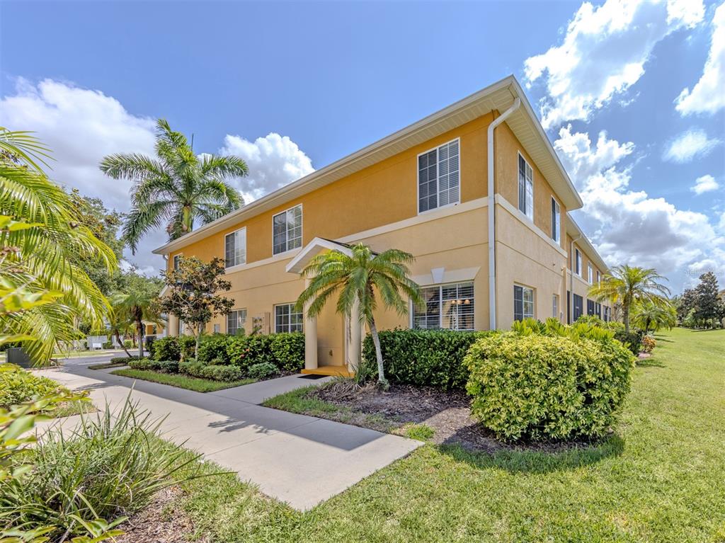 A two-story yellow apartment building with a palm tree and sidewalk in the foreground — 12983 TIGERS EYE DRIVE, VENICE, FL