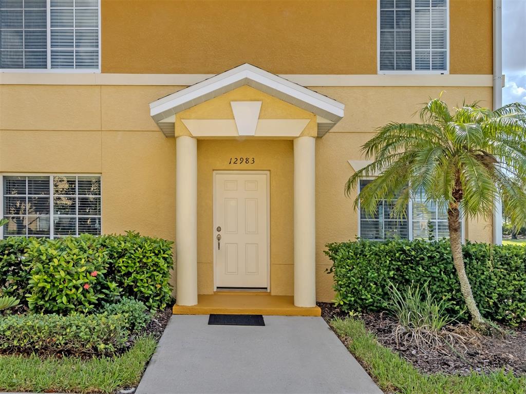 The exterior of a yellow building features a white front door under a covered entryway — 12983 TIGERS EYE DRIVE, VENICE, FL