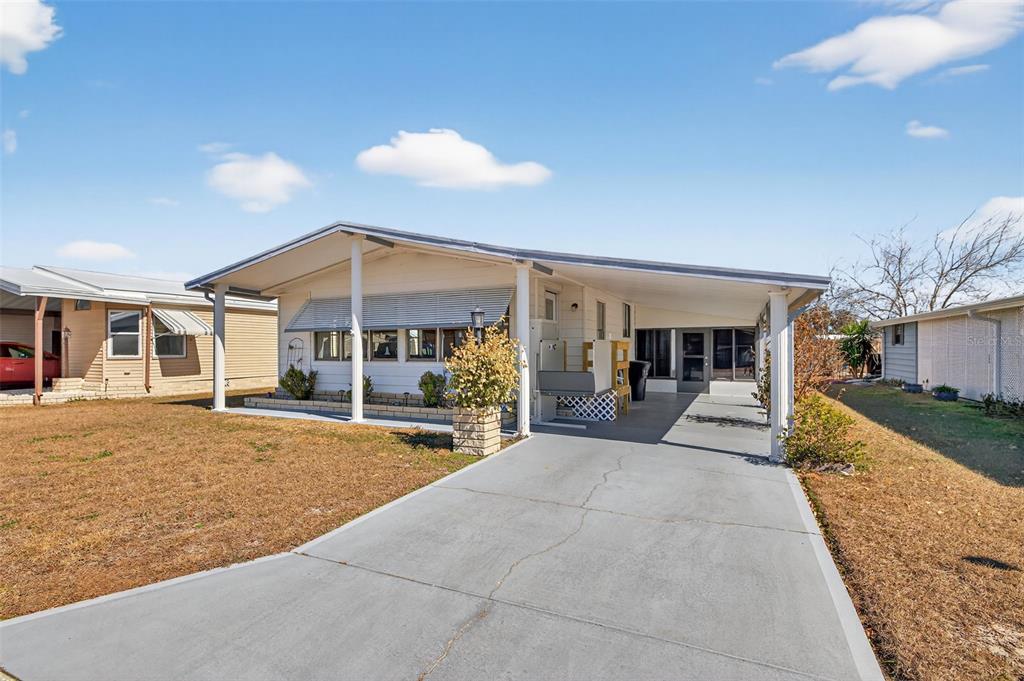 A single-story mobile home with a concrete driveway, carport, and a small front yard — 3836 WILLIAM HUME DRIVE, ZEPHYRHILLS, FL