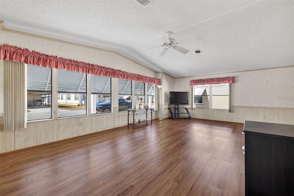 A living room with wood-look flooring, large windows, a ceiling fan, and pink valances — 3836 WILLIAM HUME DRIVE, ZEPHYRHILLS, FL