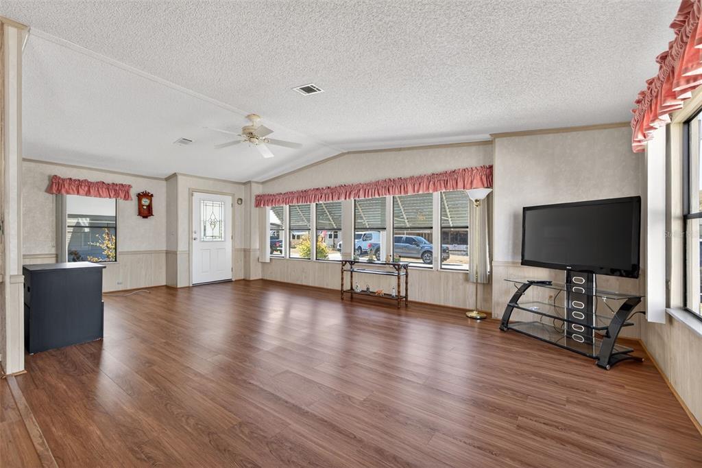 A spacious living room features wood-look flooring, a vaulted ceiling, and a wall of windows — 3836 WILLIAM HUME DRIVE, ZEPHYRHILLS, FL
