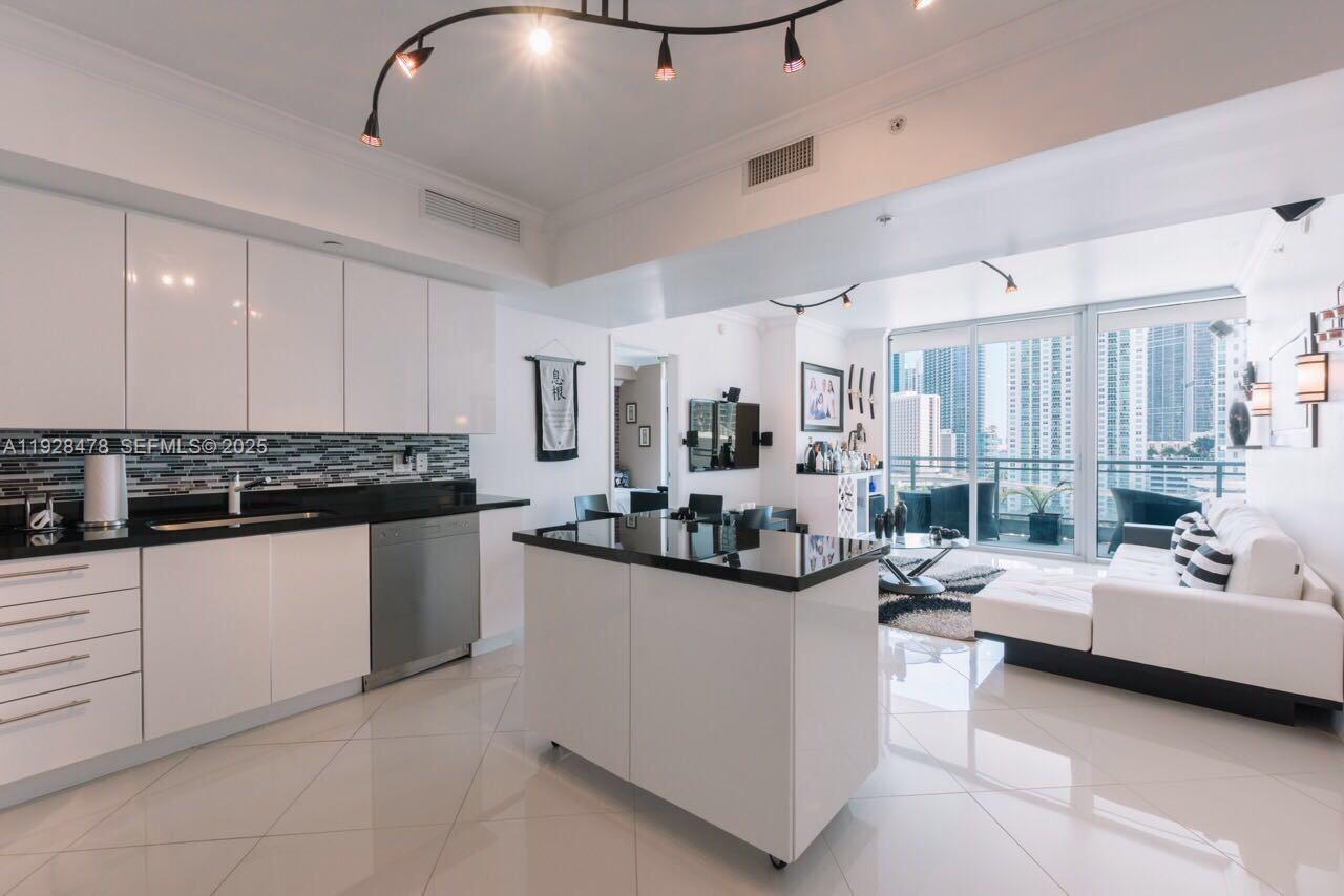 A modern kitchen with white cabinets and black countertops opens into a bright living area — 92 SW 3RD St # 1512, Miami FL 33130, MIAMI, FL