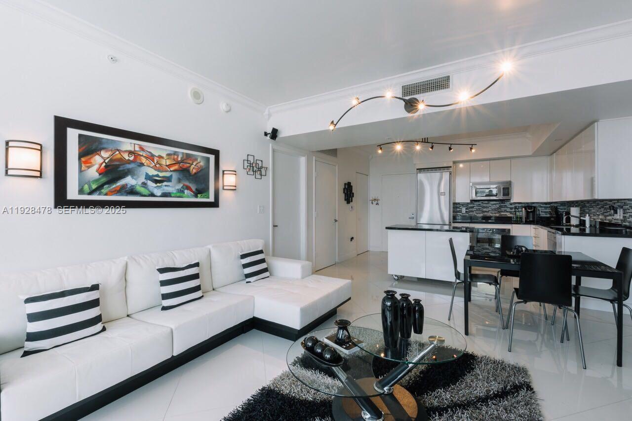 A modern living room and kitchen area feature white leather furniture, black accents, and tile flooring — 92 SW 3RD St # 1512, Miami FL 33130, MIAMI, FL